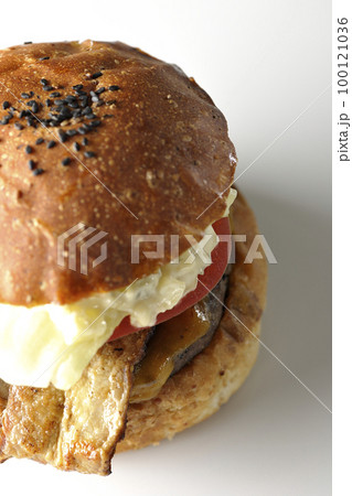 タルタルソースがはみ出ててベーコンとレタスとトマトがはさまったBLTバーガーを白背景で撮影 100121036