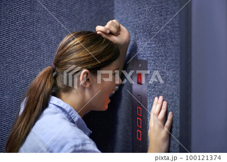 Im stuck in here. Shot of a fearful woman shouting into an elevator intercom. Im stuck in here. Shot of a fearful woman shouting into an elevator intercom. 100121374