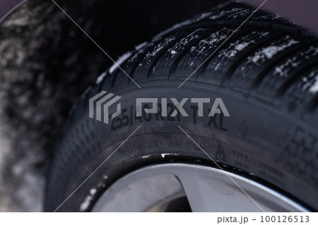 Close up view of snowy tire with tire width, height and wheel diameter designation. Winter tire size types labels. 100126513