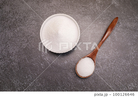 Organic sweetener Erythritol, produced by fermentation from corn, called dextrose in ceramic bowl, wooden spoon on granite background, table. Sugar substitute. Horizontal plane, top view, copy space 100126646