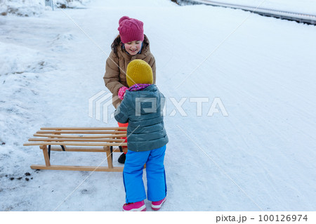 elder sister helping yonger sister on snow slope with wooden sleigh elder sister helping yonger sister on snow slope with wooden sleigh 100126974