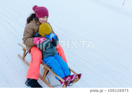 two children sledding on snow slope at wooden sleigh two children sledding on snow slope at wooden sleigh 100126975