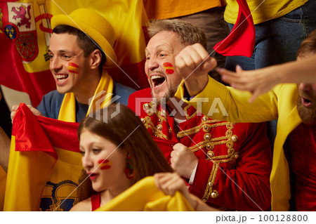 Live game. People, football, soccer fans emotionally watching match, cheering up favourite team. Fans wearing colorful scarves and flags Live game. People, football, soccer fans emotionally watching match, cheering up favourite team. Fans wearing colorful scarves and flags 100128800
