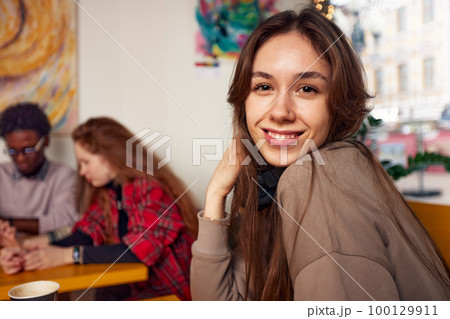 A cute girl poses for the camera in a coffee shop against the background of talking people. 100129911