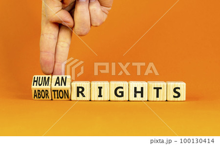Abortion rights symbol. Concept words Abortion rights are human rights on wooden cubes. Businessman hand. Beautiful orange table orange background. Business medical abortion rights concept. Copy space Abortion rights symbol. Concept words Abortion rights are human rights on wooden cubes. Businessman hand. Beautiful orange table orange background. Business medical abortion rights concept. Copy space 100130414