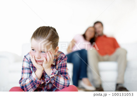 I hate timeout. A little girl sits and sulks while her parents in the background. I hate timeout. A little girl sits and sulks while her parents in the background. 100131053