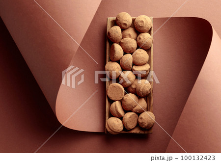 Tasty chocolate truffles in a wooden dish on a brown background. 100132423