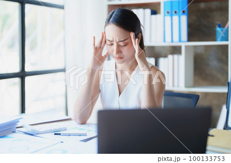 Portrait of a young Asian woman showing acute headache from sitting for a long time at work 100133753