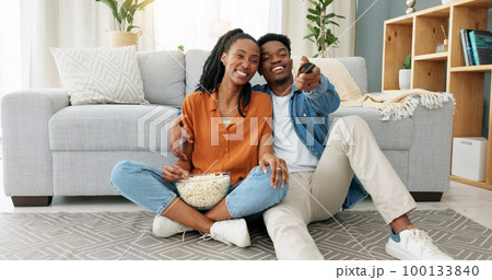 Happy black couple, eating popcorn and a movie playing in the living room of their home or house. Love, romance and man and woman having leisure time while looking at tv and browsing channels. Happy black couple, eating popcorn and a movie playing in the living room of their home or house. Love, romance and man and woman having leisure time while looking at tv and browsing channels. 100133840