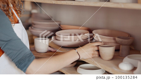 Pottery woman, shelf and creative ceramic cups with artist or craft person standing in artisan workshop or art studio. Entrepreneur potter female enjoy hobby making art to sell in startup business 100135284