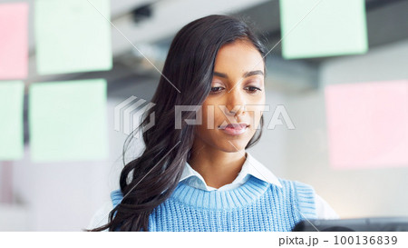 Focused young business woman thinking while brainstorming solutions for a project and marketing strategy in a creative startup agency. Designer planning ideas and information on a window in an office 100136839