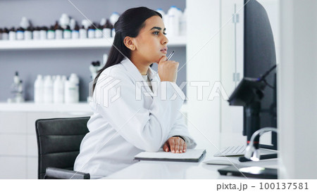 Young scientist using a computer and microscope in a lab. Female pathologist analyzing medical samples while doing experiments to develop a cure. Microbiologist conducting forensic research 100137581