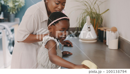 Little girl helping her mother with household chores at home. Happy mom and daughter wearing gloves while spraying and scrubbing the kitchen counter together. Kid learning to be responsible by doing Little girl helping her mother with household chores at home. Happy mom and daughter wearing gloves while spraying and scrubbing the kitchen counter together. Kid learning to be responsible by doing 100138794
