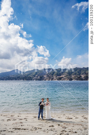 青空の海で楽しそうにする新郎新婦 100139200