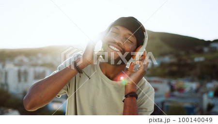 Man, music and dancing on rooftop with headphones in sunshine, city and summer with smile. Happy, black man and streaming to listen on internet, web or app to relax, dance and radio in Cape Town 100140049