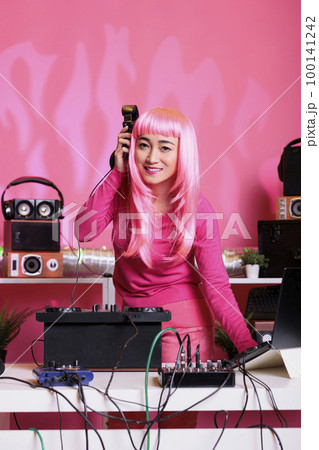 Asian performer dancing while playing techno music at professional turntables while having fun with fans in club during night time. Dj artist performing song using professional audio equipment Asian performer dancing while playing techno music at professional turntables while having fun with fans in club during night time. Dj artist performing song using professional audio equipment 100141242