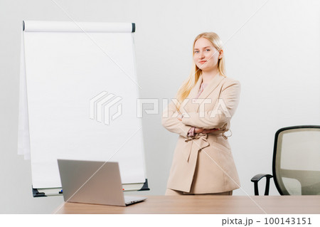 a blonde in a suit in an office with a board for meetings, desktop and laptop 100143151