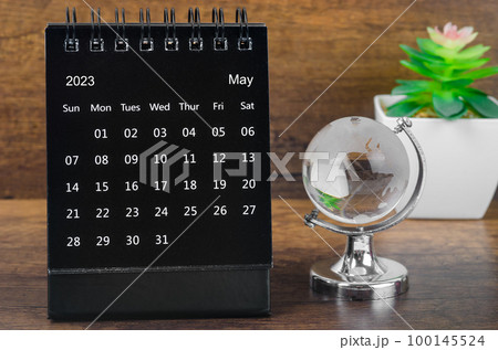 The May 2023 desk calendar for 2023 year Black color with a crystal globe against a wooden table background. 100145524