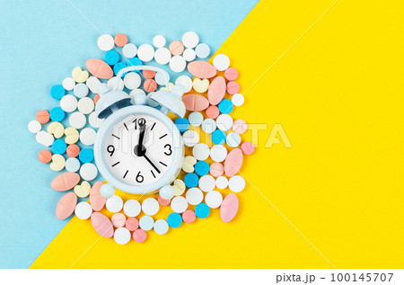 The pills and alarm clock on the blue and yellow color background 100145707