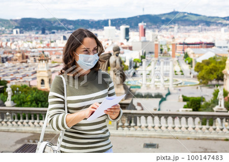 Traveling girl in protective mask looking at the guide in city european street Traveling girl in protective mask looking at the guide in city european street 100147483