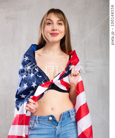 Flirting young woman with American flag against gray wall indoors Flirting young woman with American flag against gray wall indoors 100148556