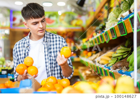 Concentrated guy buyer chooses oranges on the counter Concentrated guy buyer chooses oranges on the counter 100148627