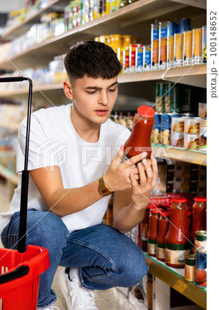 Guy reading label on bottle with tomato juice in supermarket 100148652