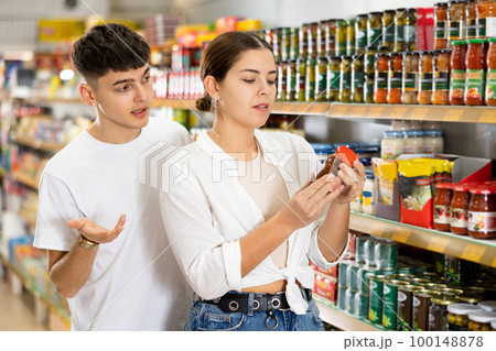 Focused interested young couple choosing sauce in supermarket Focused interested young couple choosing sauce in supermarket 100148878