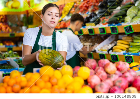 Friendly female vendor laying out ripe melon on counter Friendly female vendor laying out ripe melon on counter 100148909