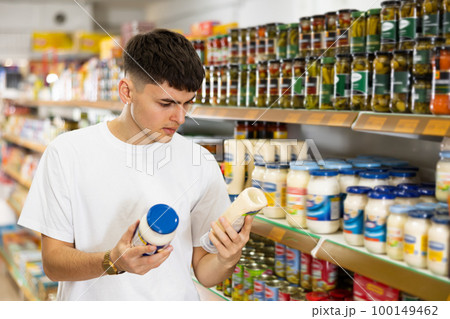 Interested guy reading label of jar of mayonnaise in supermarket Interested guy reading label of jar of mayonnaise in supermarket 100149462