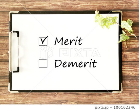 クリップボードに挟んだ白い用紙_茶色木板背景_横_MeritとDemeritの文字入り 100162246