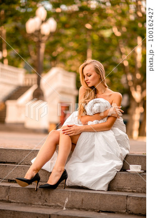 Woman city blanket. Morning in the big city. A blonde woman in a white blanket is enjoying in the city center. Photographed for social media Woman city blanket. Morning in the big city. A blonde woman in a white blanket is enjoying in the city center. Photographed for social media 100162427