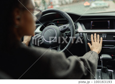 Female driver is controlling car air conditioning system grid panel on console while driving in city 100163193