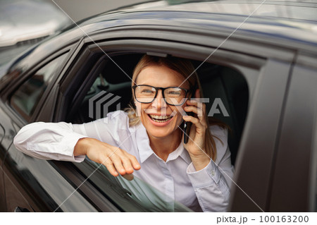 Smiling businesswoman traveling on back seat of car and talking smartphone while looking at window  100163200