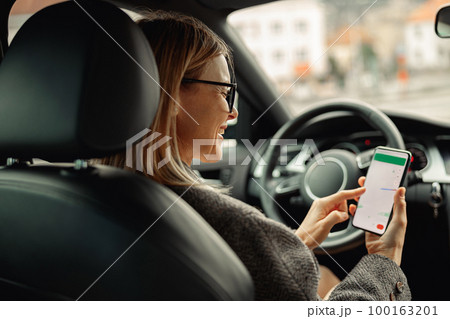 Female driver in glasses using phone with gps navigation app on screen while traveling by car Female driver in glasses using phone with gps navigation app on screen while traveling by car 100163201