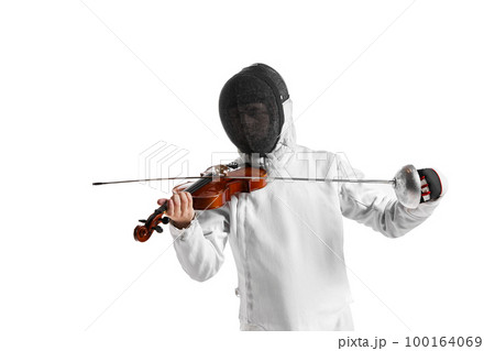 Young man, male fencer in fencing costume and protective mask helmet playing violin over white background. Concept of sport, music, hobbies 100164069