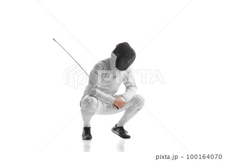 Full-length portrait of sportive man, professional fencer in fencing costume and protective helmet mask have rest isolated on white studio background. 100164070