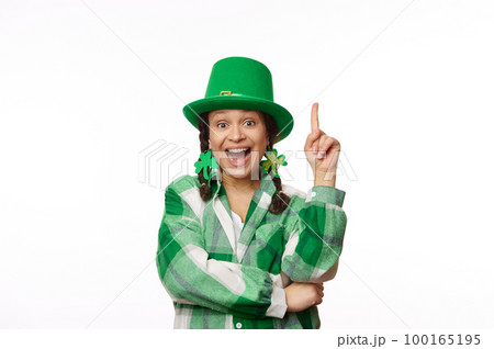 Amazed dark-haired multi-ethnic pretty woman in green carnival clothes for St. Patrick's pub party, pointing her index finger up at copy space for ads on white background. Irish culture and traditions 100165195