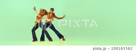 Incendiary dance. Emotional man and woman in retro style clothes dancing disco dance over green background. Concept of fashion trends of 70s, 1980s years, music Incendiary dance. Emotional man and woman in retro style clothes dancing disco dance over green background. Concept of fashion trends of 70s, 1980s years, music 100165562