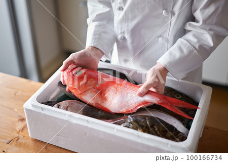 産地から届いたされた魚を手に取るシェフ 100166734