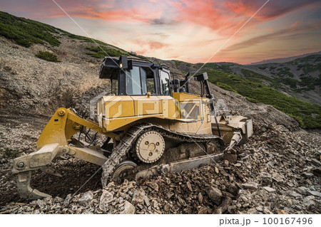 Yellow excavator on new construction site, with the bright sun and nice red sky in the background 100167496
