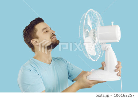 Happy man enjoying cool, fresh air blowing from an electric fan on a hot summer day Happy man enjoying cool, fresh air blowing from an electric fan on a hot summer day 100168257