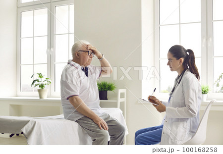 Senior man patient complaining on headache to attentive woman doctor in modern clinic hospital. 100168258