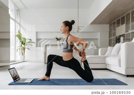 Young woman doing fitness in her apartment with laptop 100169330