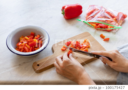 woman's hands cutting fresh bell peppers and putting them in a freezer bag 100175427