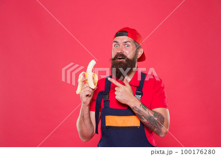 Hungry hipster. Favorite snack. Food court. Lunch time. Bearded man in uniform and cap eating banana. Worker builder mechanic eat banana. Fresh fruit. Living healthy life. Tasty food. Bite banana Hungry hipster. Favorite snack. Food court. Lunch time. Bearded man in uniform and cap eating banana. Worker builder mechanic eat banana. Fresh fruit. Living healthy life. Tasty food. Bite banana 100176280