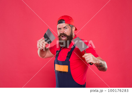 Professional plasterer. Skillful plasterer. Successful renovation. Repair success. Plasterer hipster builder in cap red background. Interior designer. Bearded man worker with plastering tools Professional plasterer. Skillful plasterer. Successful renovation. Repair success. Plasterer hipster builder in cap red background. Interior designer. Bearded man worker with plastering tools 100176283