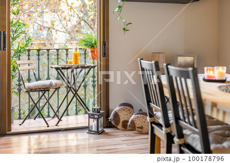 View from the living room to balcony with a table and stylish decor elements with coffee table and a chair with orange juice overlooking the trees with an autumn landscape. Luxury apartment concept 100178796