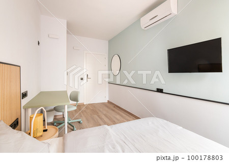 Empty light room with bed, desk, desk and air-conditioner and TV on light green and white wall background. Concept of luxury hotel room or room for a young couple Empty light room with bed, desk, desk and air-conditioner and TV on light green and white wall background. Concept of luxury hotel room or room for a young couple 100178803
