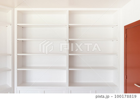 Large wooden closed mahogany door with a brass handle for opening. Along the wall is a white open cabinet with shelves for books and interior items for coziness and comfort. The floor is parquet. Large wooden closed mahogany door with a brass handle for opening. Along the wall is a white open cabinet with shelves for books and interior items for coziness and comfort. The floor is parquet. 100178819